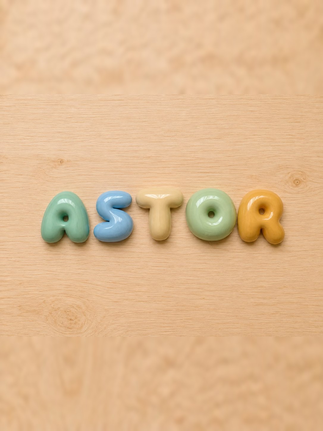 Nombre Astor en letras bubble verde mar, azul mar, albaricoque, verde bebé y amarillo arena sobre madera clara