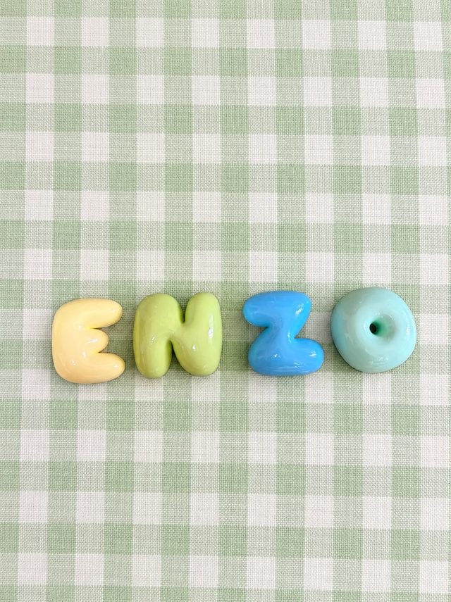 Nombre Enzo en letras bubble amarillo, verde y azul sobre un mantel de cuadros verde