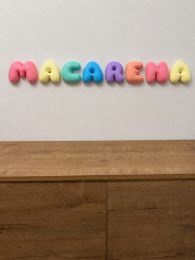 Nombre Macarena en letras bubble arcoíris pastel colgado en la pared sobre un mueble de madera