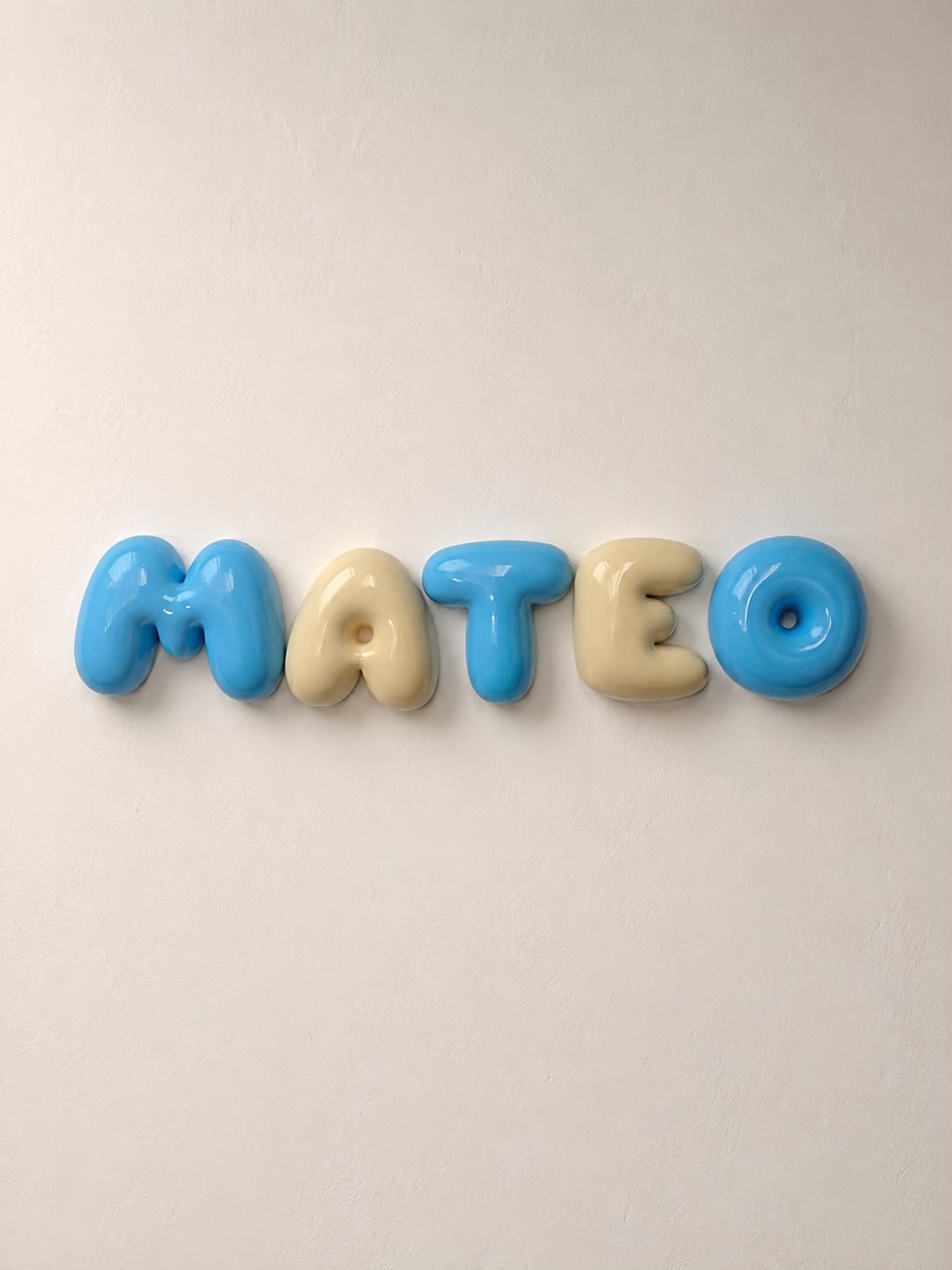 Nombre Mateo en letras bubble azul claro y albaricoque claro alternados en una pared blanca